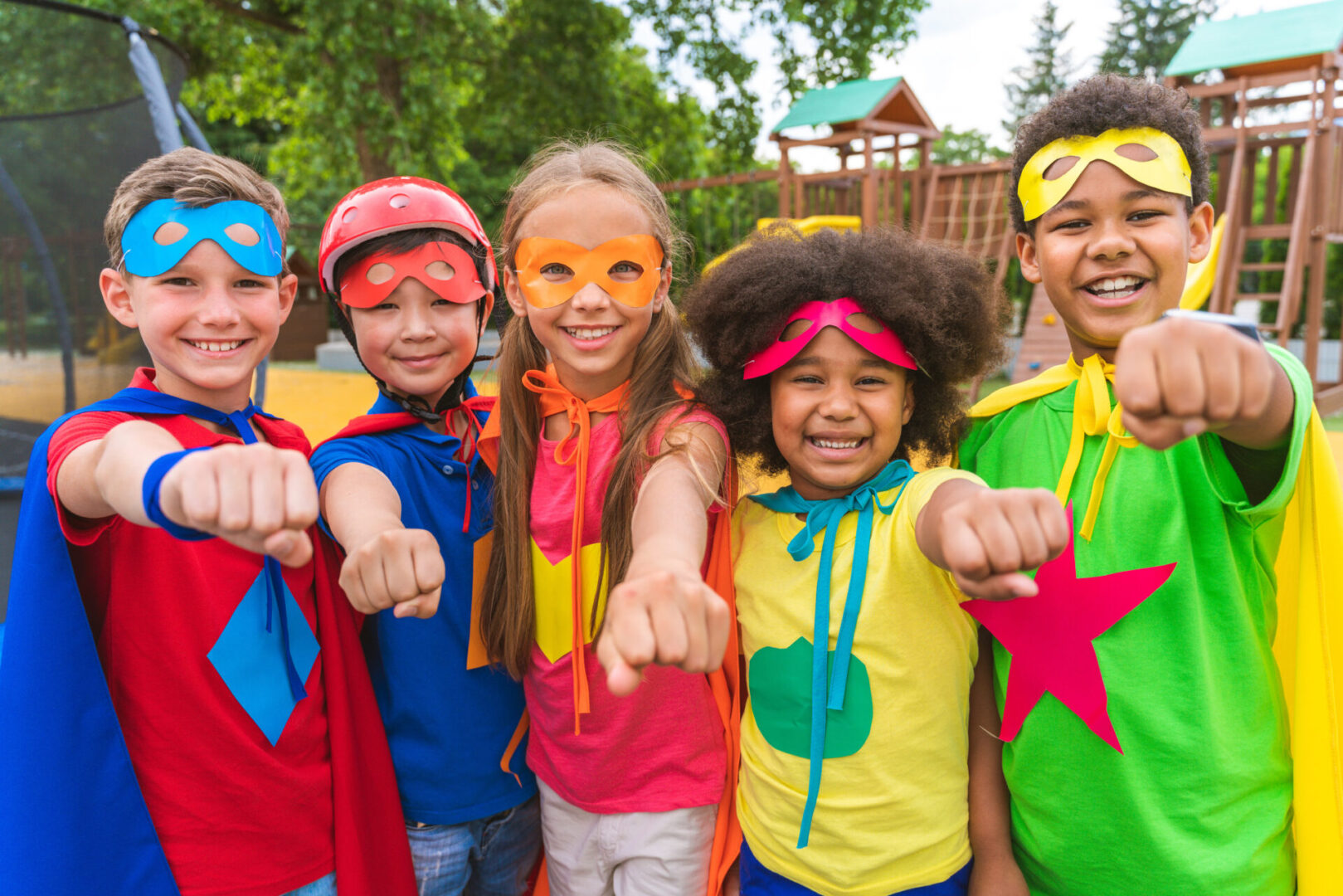 Multiracial group of young schooler wearing superhero costumes and having fun outdoors